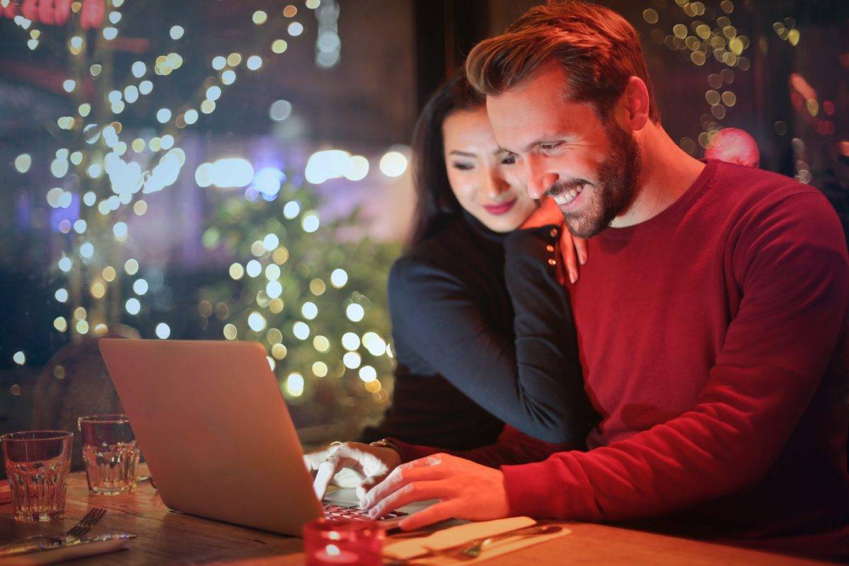 man and woman happy looking at computer with Christmas lights in background